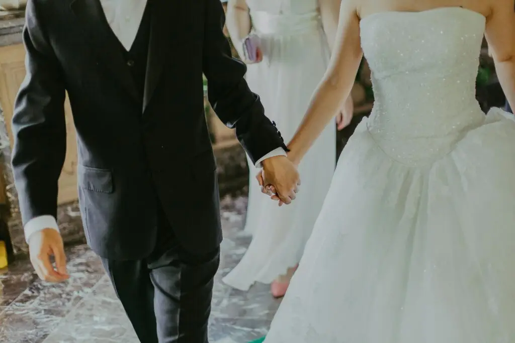 pexels photo 1043902 1043902 A romantic moment capturing a bride and groom holding hands in elegant wedding attire indoors.